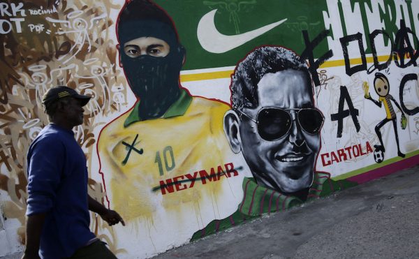 A man walks in front of mural covered in graffiti featuring Brazil's Neymar which has been modified to make the Barcelona striker look like a member of the Black Blocs, which have been active in Brazil's ongoing protest movement against the World Cup, in Rio de Janeiro, Brazil, Tuesday, May 27, 2014. Teams from 32 nations will compete in the upcoming World Cup, with Sao Paulo hosting the opening ceremony and kick-off match between Brazil and Croatia on June 12. (AP Photo/Hassan Ammar)